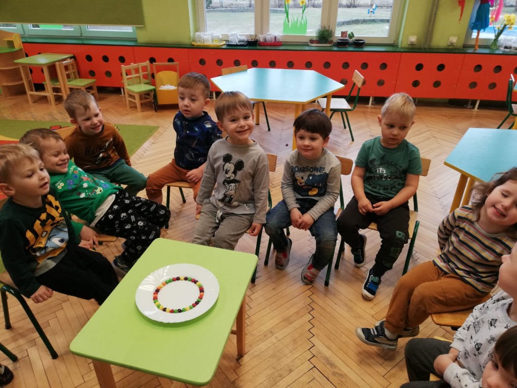 dzieci obserwują eksperyment z kolorami siedząc w kółeczku na krzesłach